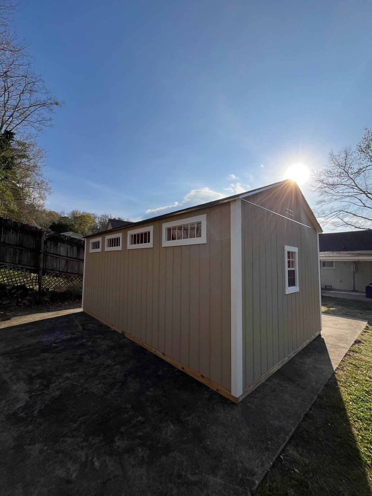 Tall tan shed with a row of transom windows down the side wall, built on-site in an Alabama backyard